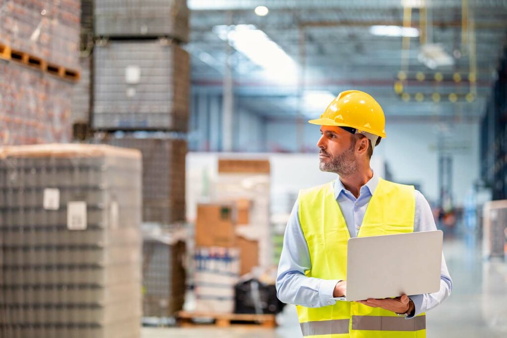 Manufacturing warehouse manager with a laptop entering inventory for lean material management